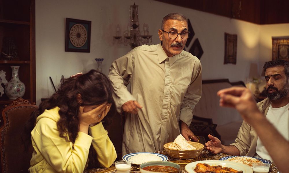 Akşam yemeği sofrasında gergin bir konuşma sırasında başını eline yaslayan genç kadın ve aile büyükleri